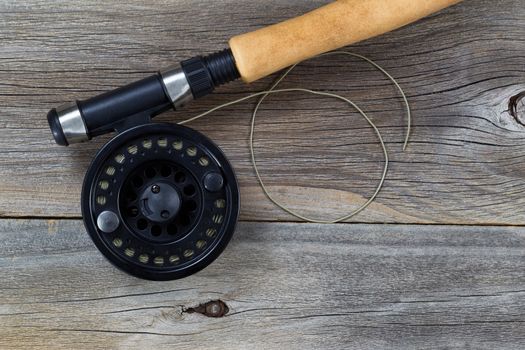 Close up of a fly reel, with line, and partial cork handled pole on rustic wood 