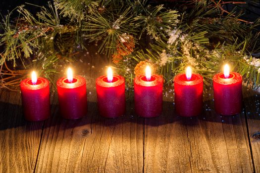 Burning red candles with snow covered evergreens and rustic wood. 