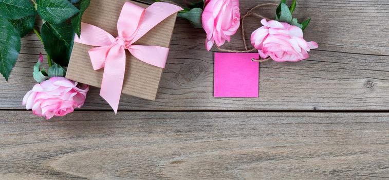 Pink roses with gift box and tag and on weathered wooden boards 