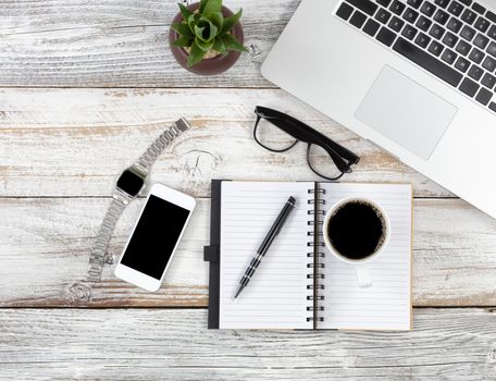 Office desktop with laptop, calendar, coffee and writing materials on white rustic desk