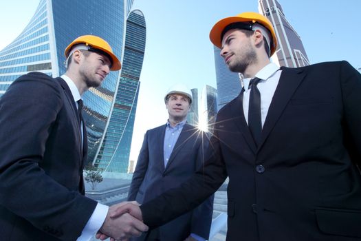 Architect and engineers shaking hands at construction site, skyscrapers on background