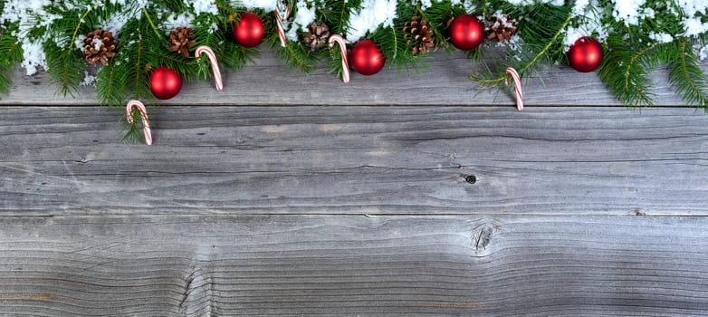 Overhead view of snow covered fir Christmas tree branches with decorations on weathered wood  