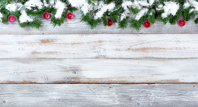 Top border of snow covered Christmas evergreen branches and red candles on white vintage wood