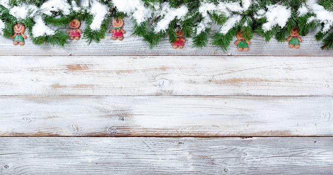 Snow covered top border of Christmas evergreen branches and cookie decorations on white vintage wood