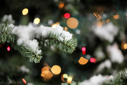 Traditional artificial Christmas tree with glowing lights and snow in background 