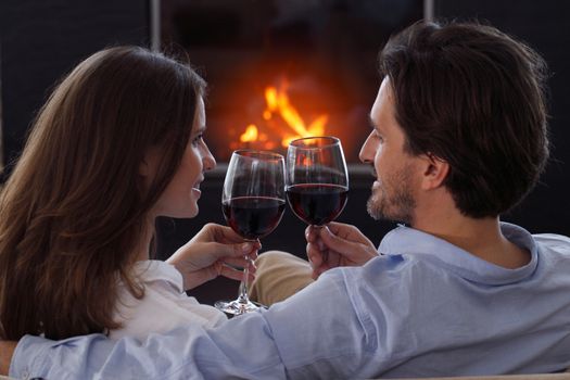Close up of young couple drinking wine in front of an open wood fire at Valentines day love passion concept