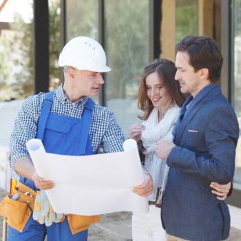 Foreman showing house design construction plan to a happy young couple new house real estate concept