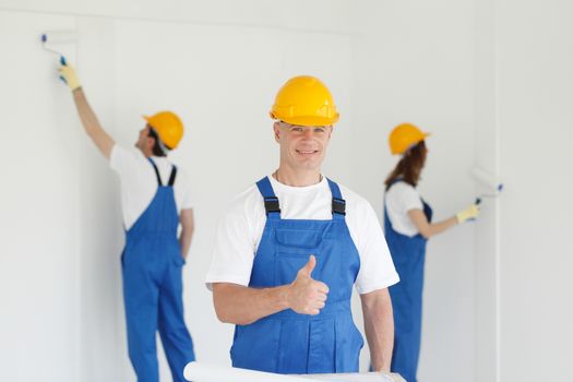 Worker gives thumb up in front of team of painters, construction, renovation concept