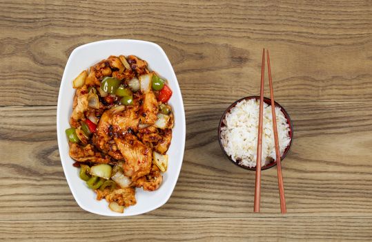 Overhead view of Chinese spicy chicken dish and rice in bowl with chopsticks placed on rustic wooden boards.  