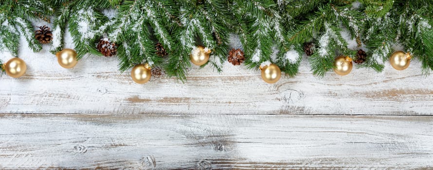 Christmas evergreen branches and golden ornaments on rustic white wood background