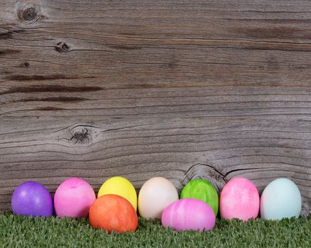 Colorful Easter egg decorations lying on grass with rustic wood in background. 