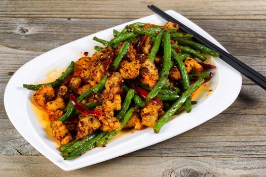 Close up view of crispy fried chicken pieces with green beans and Chile peppers on rustic wood setting. 