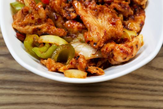 Closeup horizontal view of Chinese spicy chicken dish in white bowl with rustic wooden boards underneath 