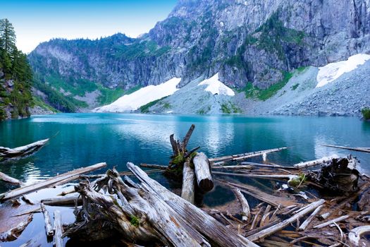 Log pile on glacier lake with mountains and snow during summer season 