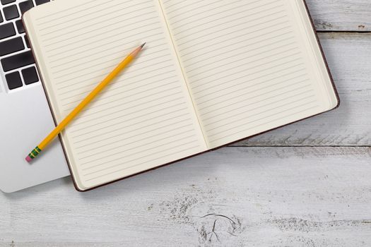 Old white wooden desk with laptop, paper notepad, and pencil. 