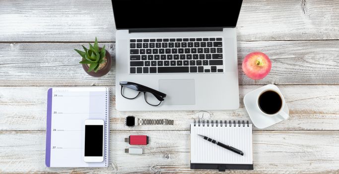 White rustic office desktop setting with laptop plus food and drink and accessories  