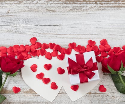 Valentines card, gift box with red heart shapes and roses on rustic white wood in flat lay view