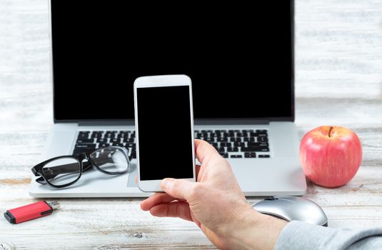 Close up of male hand holding smartphone with workstation technology in background for business or education use 