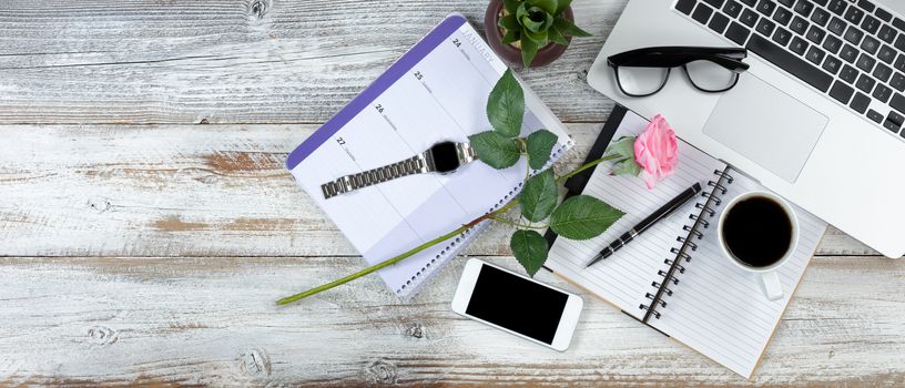 Office desktop with laptop, calendar, coffee and pink rose on white rustic desk