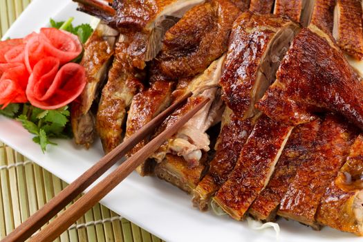 Chinese roasted duck dish with radish decoration on side of white plate