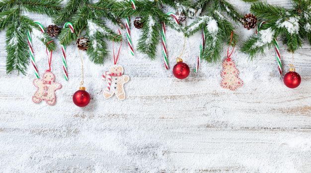 Snowy Christmas evergreen branches with hanging ornaments on rustic white wood background