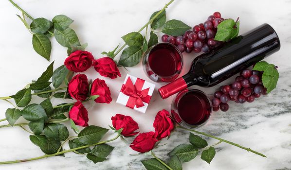 Overhead view of Red wine bottle, glasses, grapes and roses on natural marble stone setting