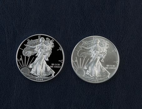 Closeup photo of a proof and uncirculated American Silver Eagle Dollar Coins side by side on dark blue vinyl holder
