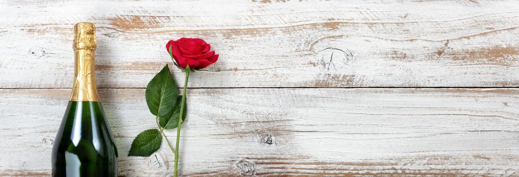 Anniversary background with red rose and champagne on white rustic wood 