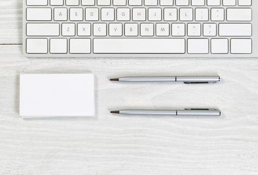 Image of partial keyboard, stack of blank business cards, and silver pens on white desktop. Layout in horizontal format.
