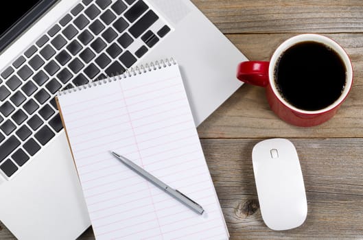 Paper and pen over laptop with coffee and mouse on side of rustic wooden desktop. 