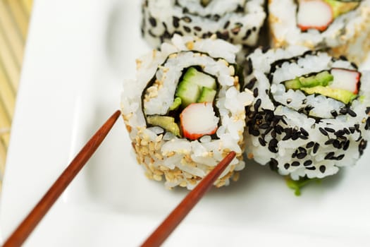 Closeup horizontal photo of a single inside out California roll being picked up with chopsticks   