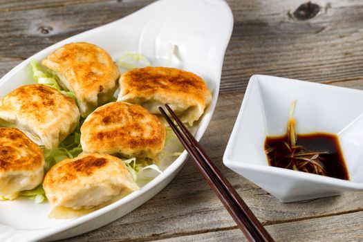 Close up of a front view of Chinese dumpling with sauce in bowl with chopsticks on rustic wood. Selective focus on tip of chopsticks. 