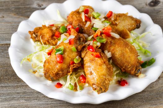 Close up view of fried chicken wings in white plate with garnishes. Rustic wood underneath.