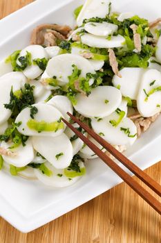 Vertical image of Chinese rice noodles with pork slices in white plate with natural bamboo background 