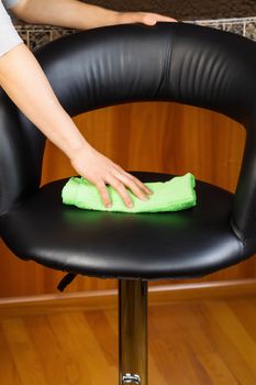 Vertical photo of female hand cleaning kitchen leather chair with green microfiber rag with red oak floor and Center Island in background 