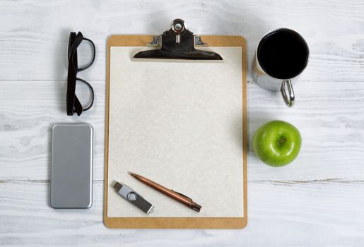 Top view of clipboard with coffee, pen, paper, apple, thumb drive, cell phone and reading glasses. 