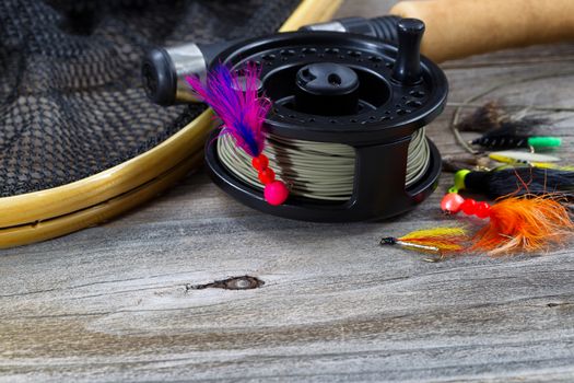 Close up of fly reel, focus on front of reel, with fly jig hanging from spool. Partial cork handled pole, net and flies blurred out on rustic wooden boards 