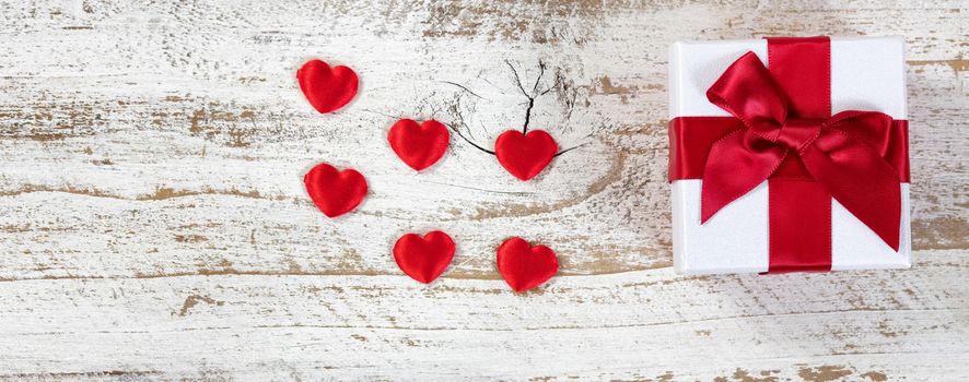 Gift box and hearts with red bow on rustic wood in flat lay view 