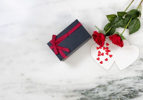 red roses and candy on card with dark gift box. Marble stone background in flat lay view 