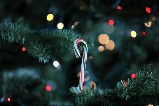 Traditional artificial Christmas tree with candy cane ornament and glowing lights in background 