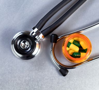 Top view of medicine bottle filled with capsules and stethoscope in background on stainless steel table 