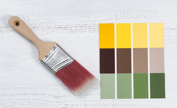 Close up of a new paint brush and paint color choice templates on white wooden boards