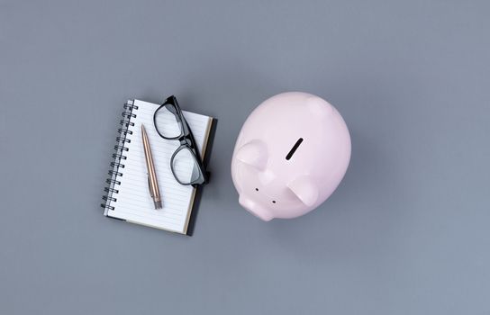 Piggy Bank and traditional writing stationery on gray desktop 