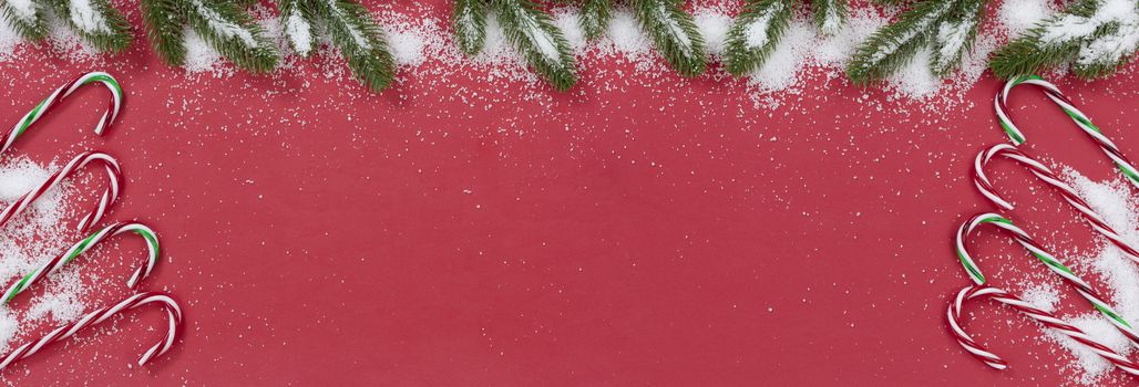 Seasonal Christmas candy cane decorations on red background with snow  