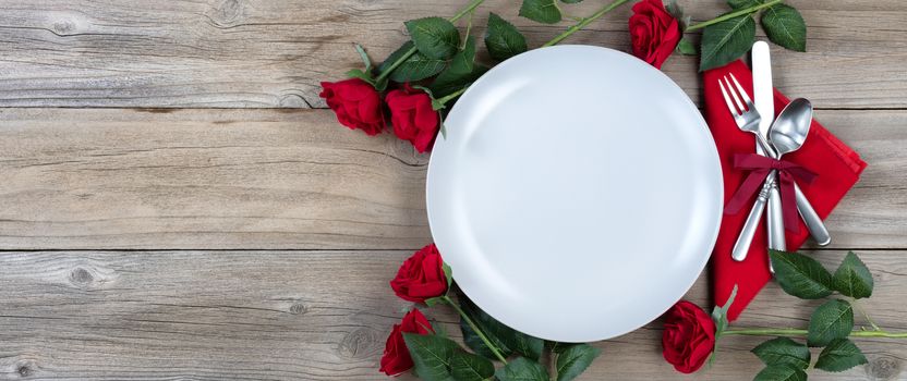 Holiday Dinner setting with red roses and silverware on rustic wood in flat lay view