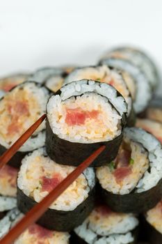 Closeup vertical photo of a single spicy tuna roll on top of sushi stack being picked up with chopsticks   