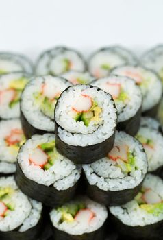 Vertical closeup photo of Single California hand roll sushi on top of pile of additional sushi 