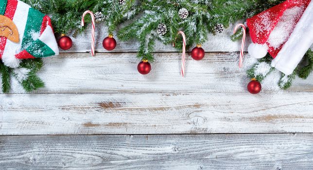 Snowy Christmas fir branches with traditional hats, red ball ornaments and pine cones on rustic wood in flat lay format