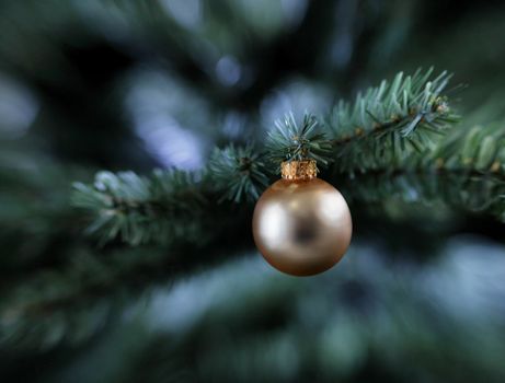 Traditional golden single Christmas ornament hanging on artificial tree 