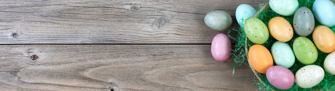 Wicker basket filled colorful eggs on weathered wooden planks for Easter background  